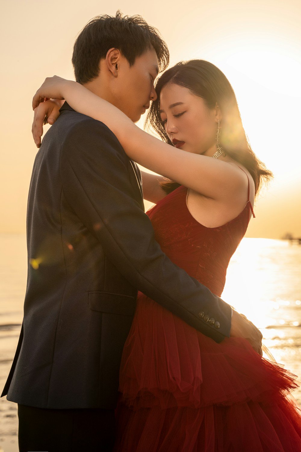 Una pareja comparte un beso en la frente frente al mar al atardecer