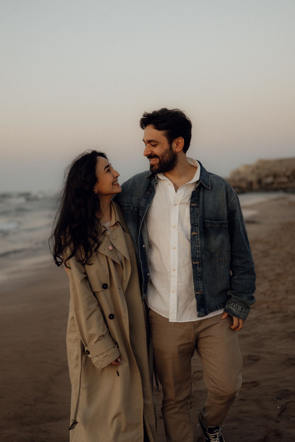 Una pareja sonríe y se mira con afecto durante un paseo por la playa